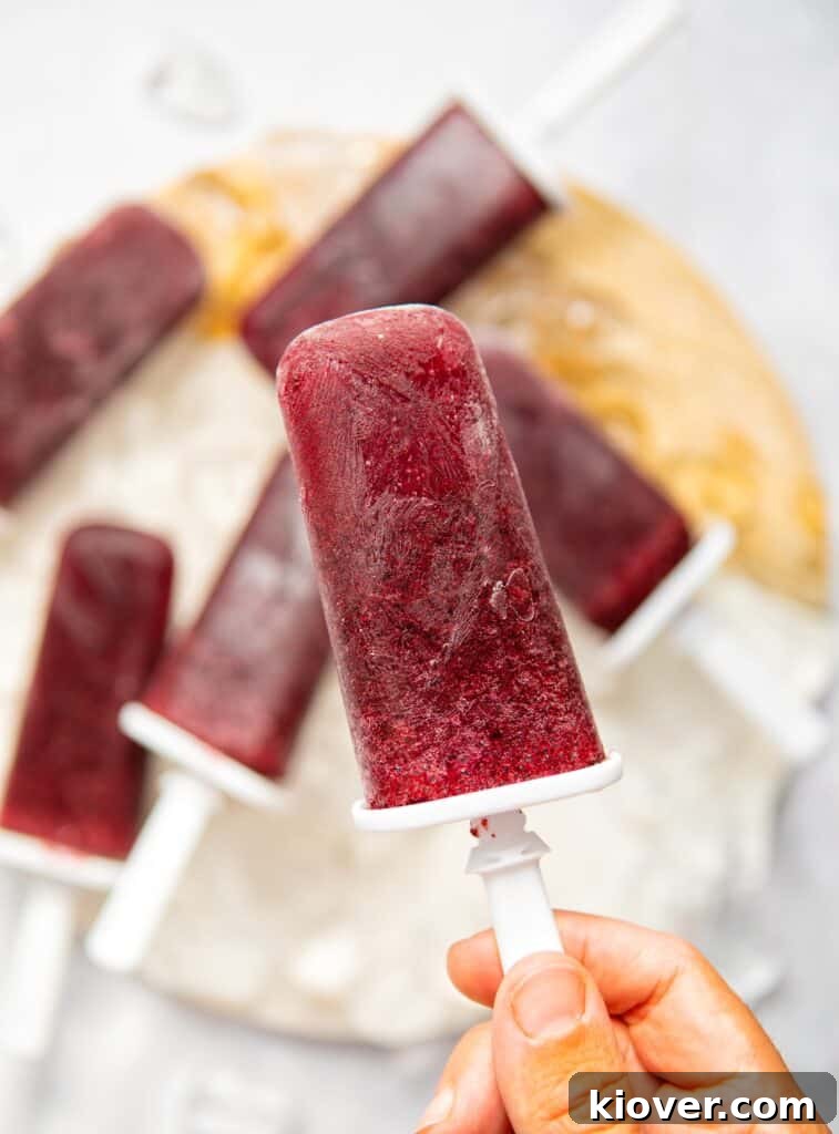 A hand holding a vibrant blueberry ice lolly, with more lollies visible in the background.