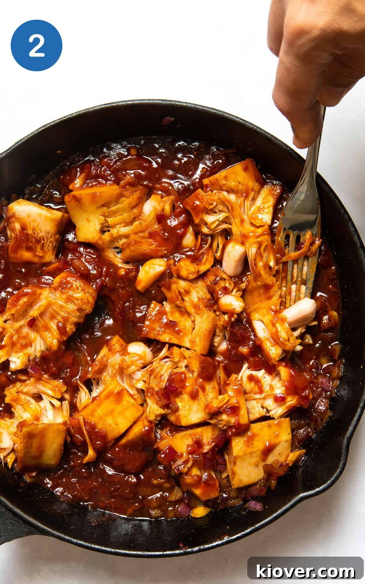 Hand pressing jackfruit in a pan with a flavorful sauce.