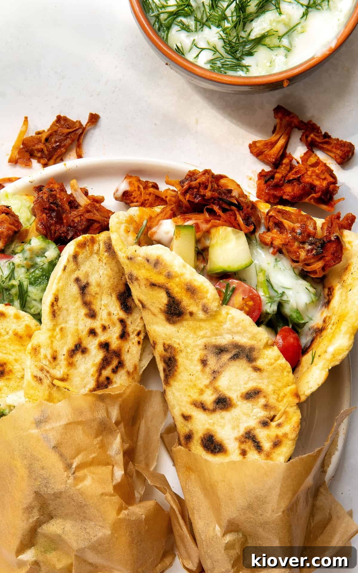 Two vegan gyros served on a plate with fresh vegetables and tzatziki.