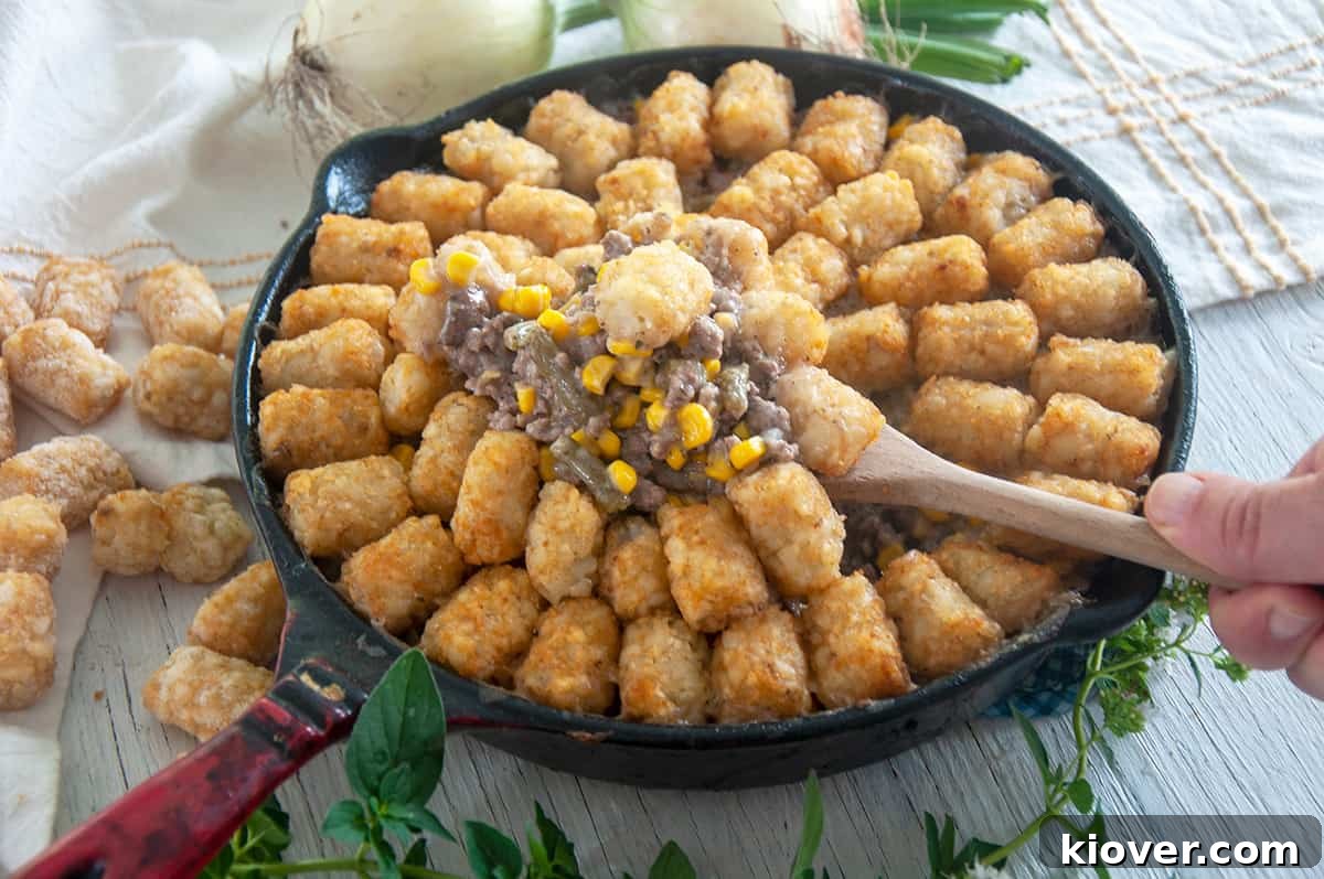 Spooning up tater tot hotdish from a cast iron skillet.