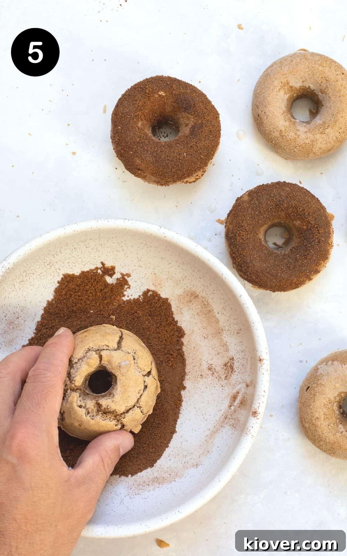 Heavenly Gluten-Free Cinnamon Baked Doughnuts 8 A baked doughnut being pressed down into a bowl of cinnamon sugar, ensuring an even coating.