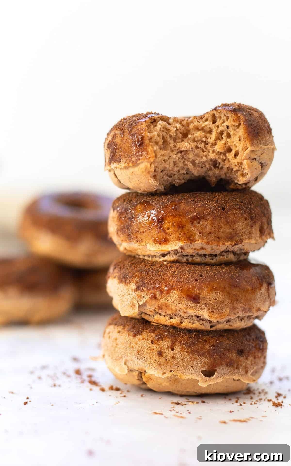 Heavenly Gluten-Free Cinnamon Baked Doughnuts 9 Four golden brown baked doughnuts stacked with a bite taken out of the top one, revealing the soft interior.