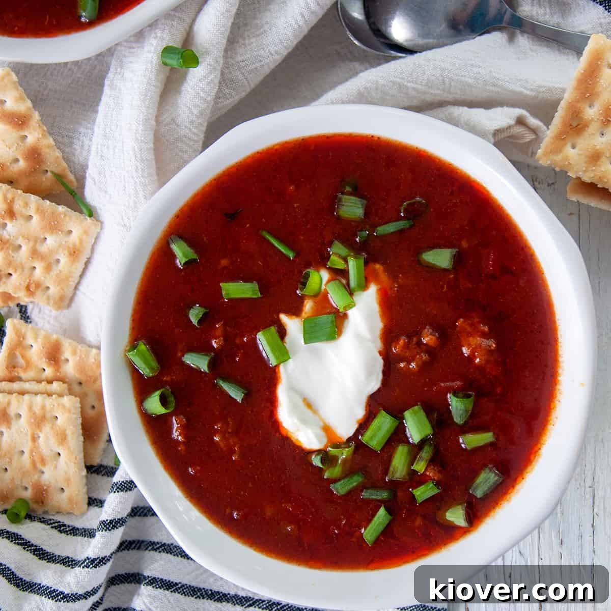 Classic Chili Con Carne in a Slow Cooker Chili con Carne in a white bowl topped with a dollop of sour cream and fresh green onions, inviting and comforting.