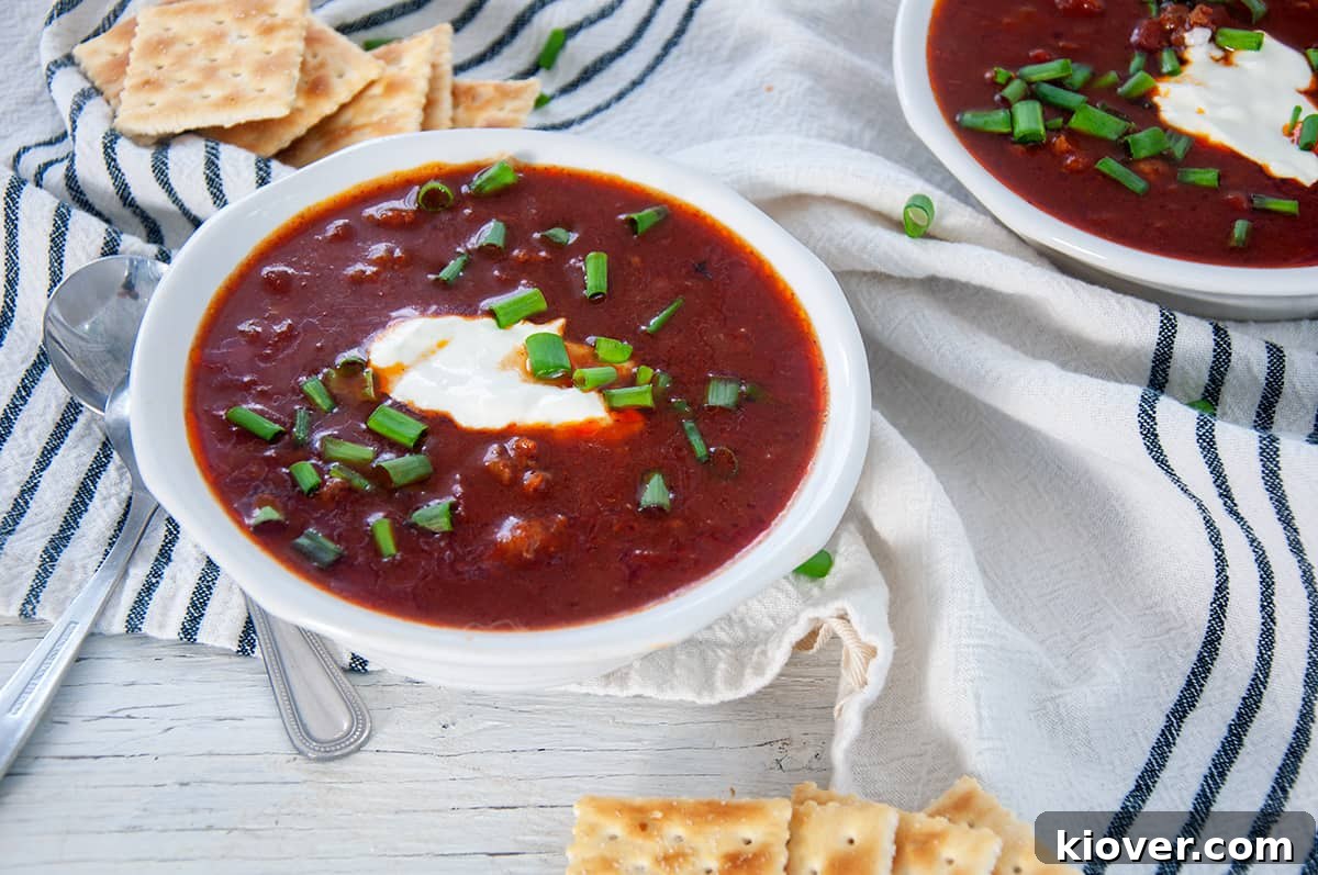 Enjoy Your Homemade Chili Con Carne A perfectly garnished bowl of chili con carne on a white table, accompanied by a small dish of sour cream and a stack of crackers, ready for enjoyment.