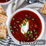 Chili con Carne in a white bowl topped with sour cream and green onions.