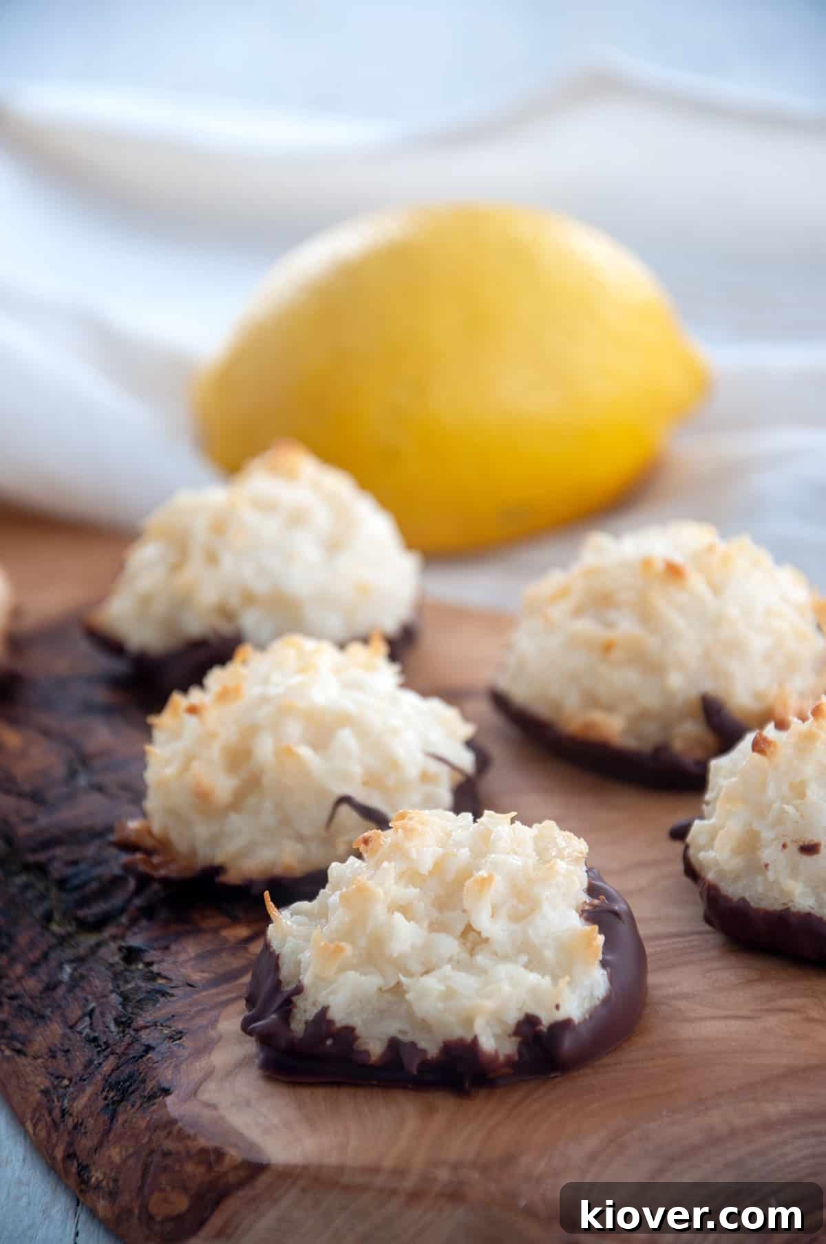 Four kokosmakronen on a wood cutting board and a lemon showing.