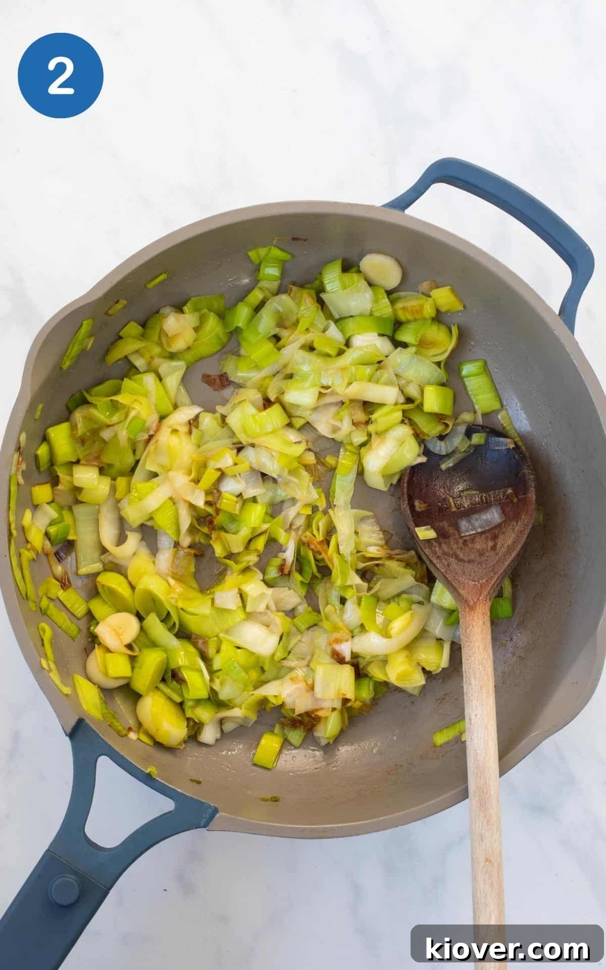 Chopped leeks gently cooking in a nonstick frying pan, stirred with a wooden spoon.