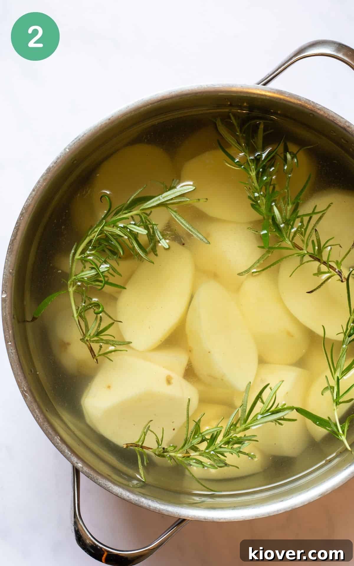 Crispy Rosemary Roasted Potatoes 5 Chopped potatoes and fresh rosemary sprigs boiling in a large pot of water on a stovetop.