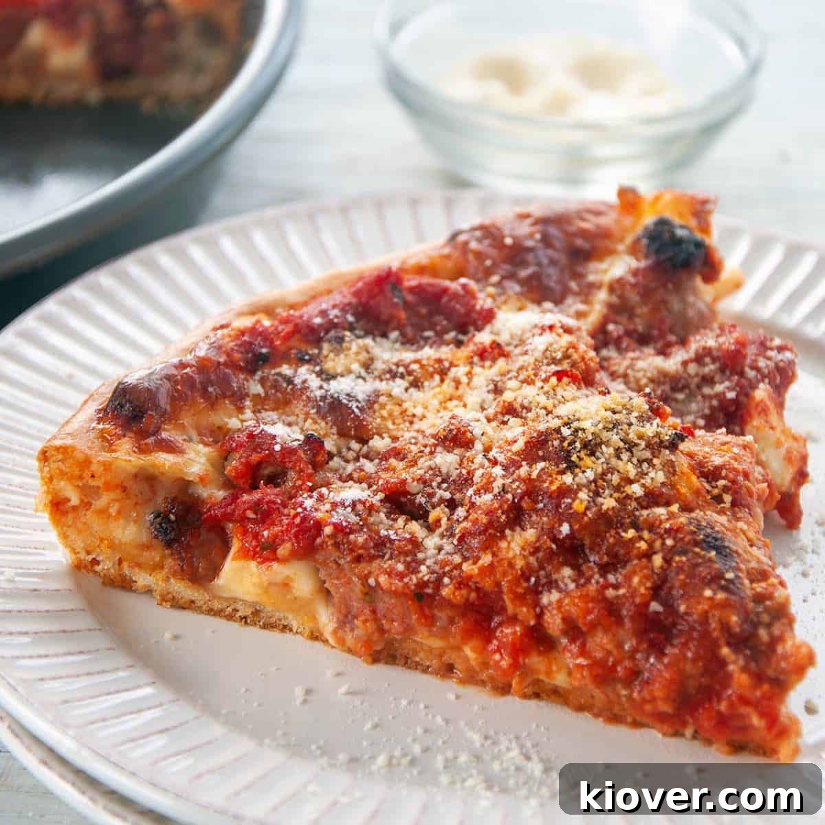 Chicago deep dish pizza A perfectly baked Chicago Deep Dish Pizza resting on a white table, with a side dish of grated cheese.