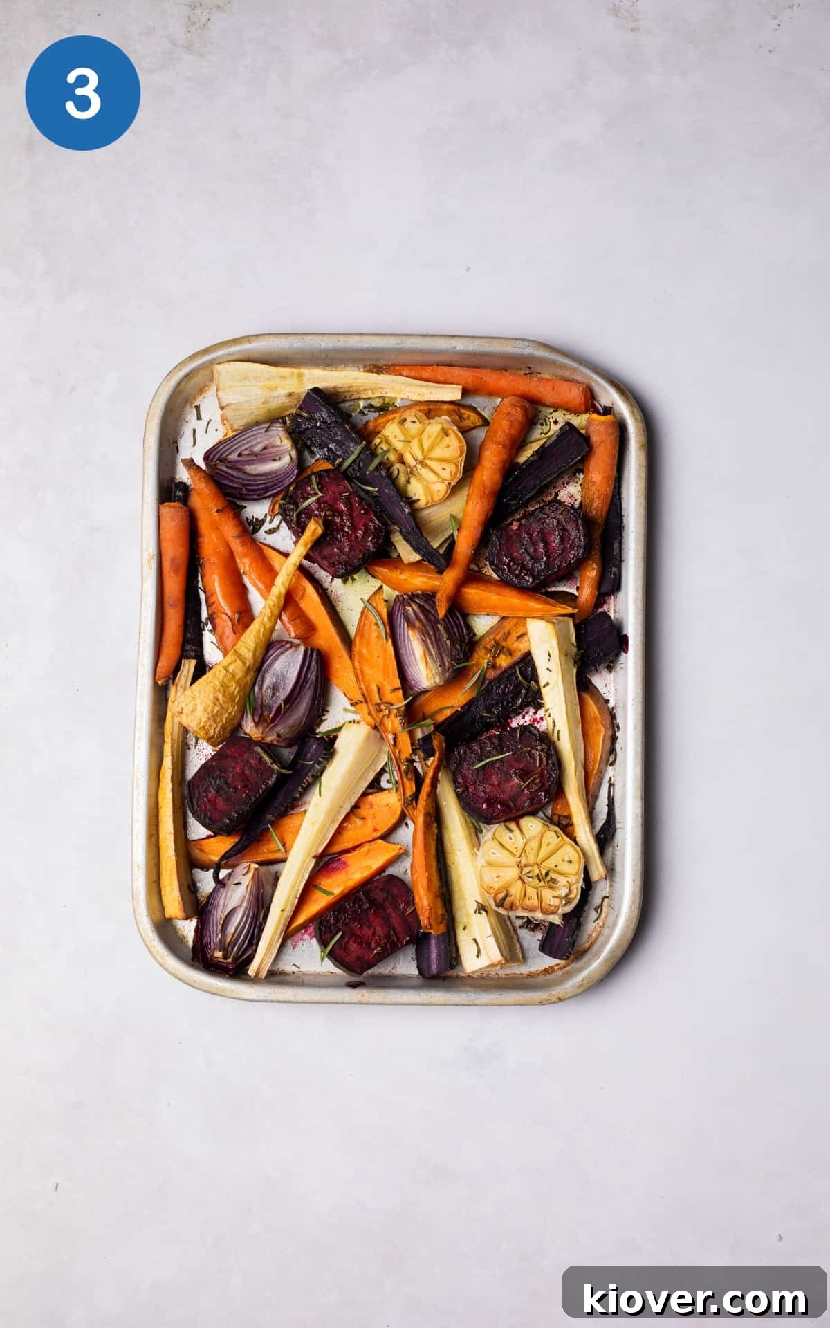 Colorful roasted root vegetables, perfectly caramelized, on a silver roasting tray.