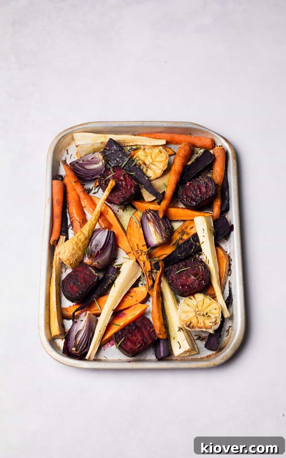 Close-up of perfectly roasted root vegetables garnished with fresh rosemary on a roasting tray.