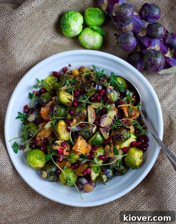Top-down view of perfectly roasted Brussels sprouts adorned with bright orange segments, crunchy walnuts, and ruby-red pomegranate seeds, in a white serving dish.