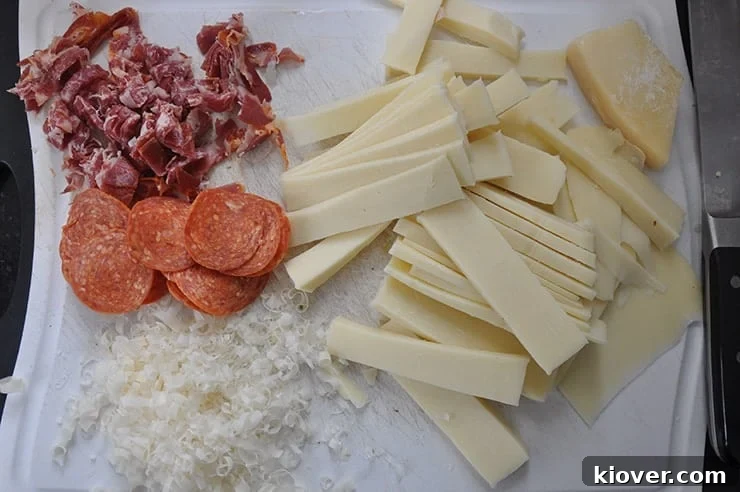 Assorted meats and cheeses laid out on a cutting board, prepped for a Chicago Deep Dish Meat Lover Pizza.