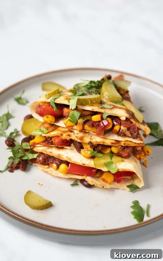 Zesty Black Bean Melts 9 Stacked black bean quesadilla wedges on a white plate, showcasing the crispy tortilla and the hearty, flavorful black bean and corn filling, garnished with fresh cilantro.