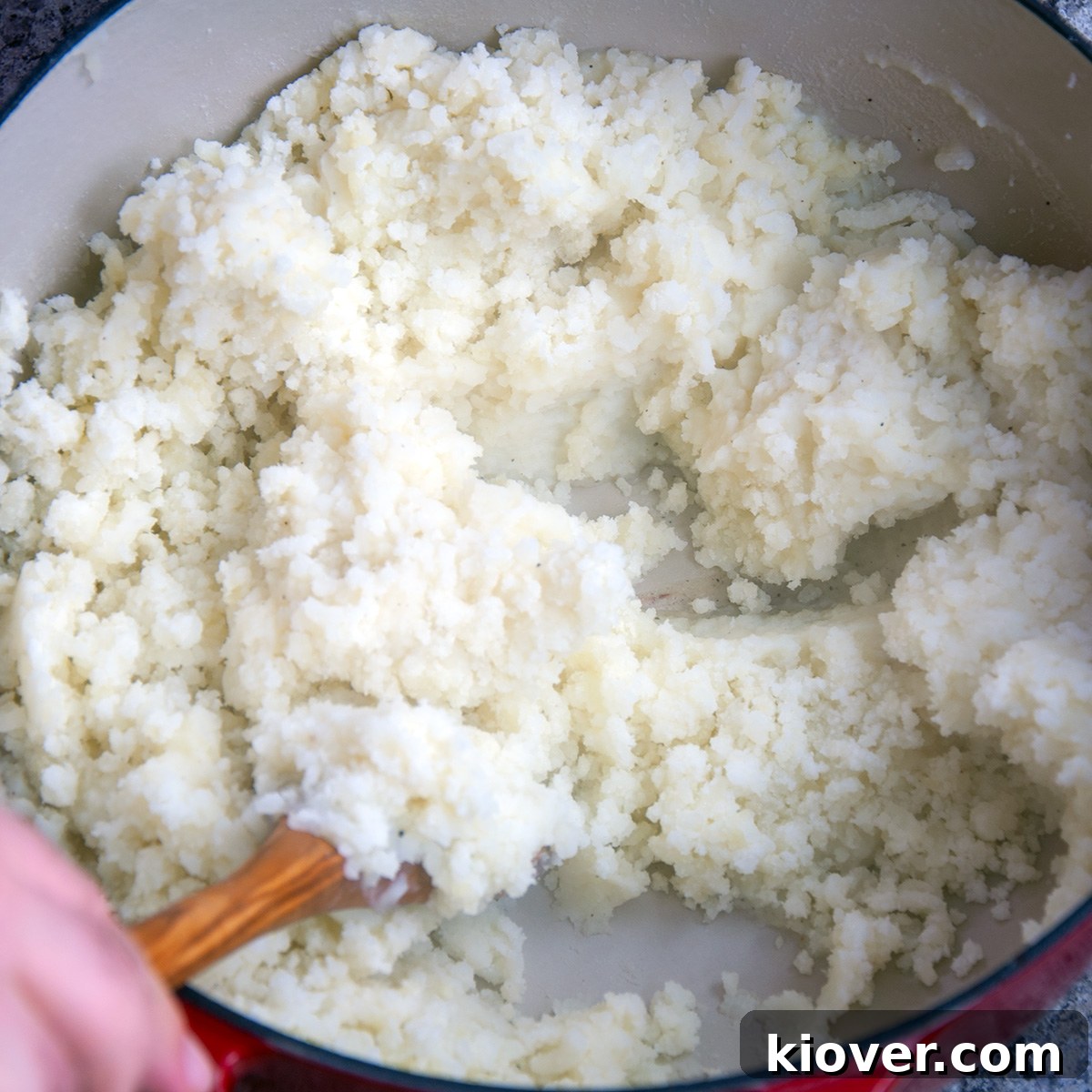 A wooden spoon gently mixing fluffy mashed potatoes in a large bowl.