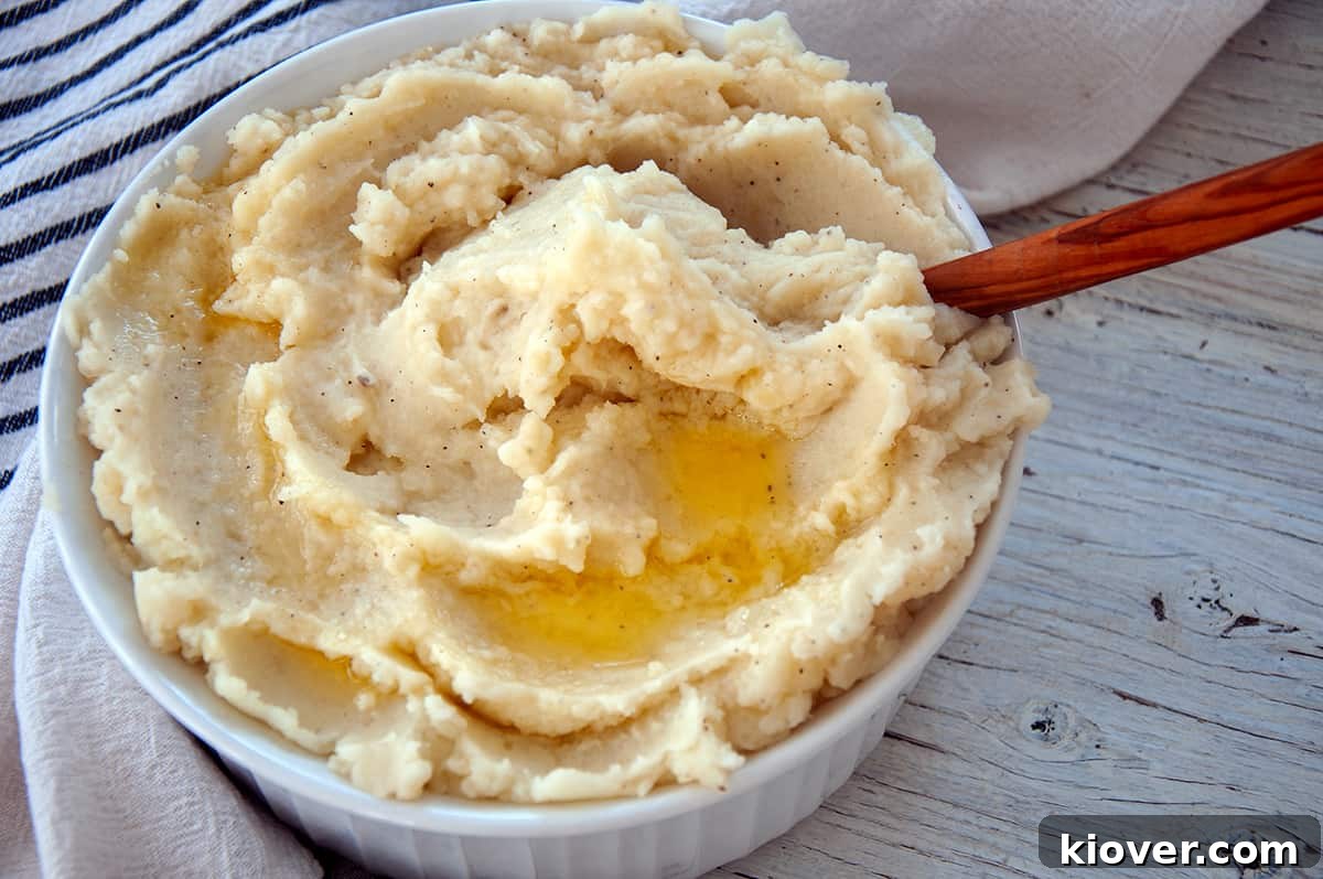 A large container of golden, fluffy mashed potatoes topped with melted butter and a wooden serving spoon.