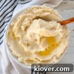 Large bowl of fluffy mashed potatoes with melted butter on top, garnished with fresh herbs.