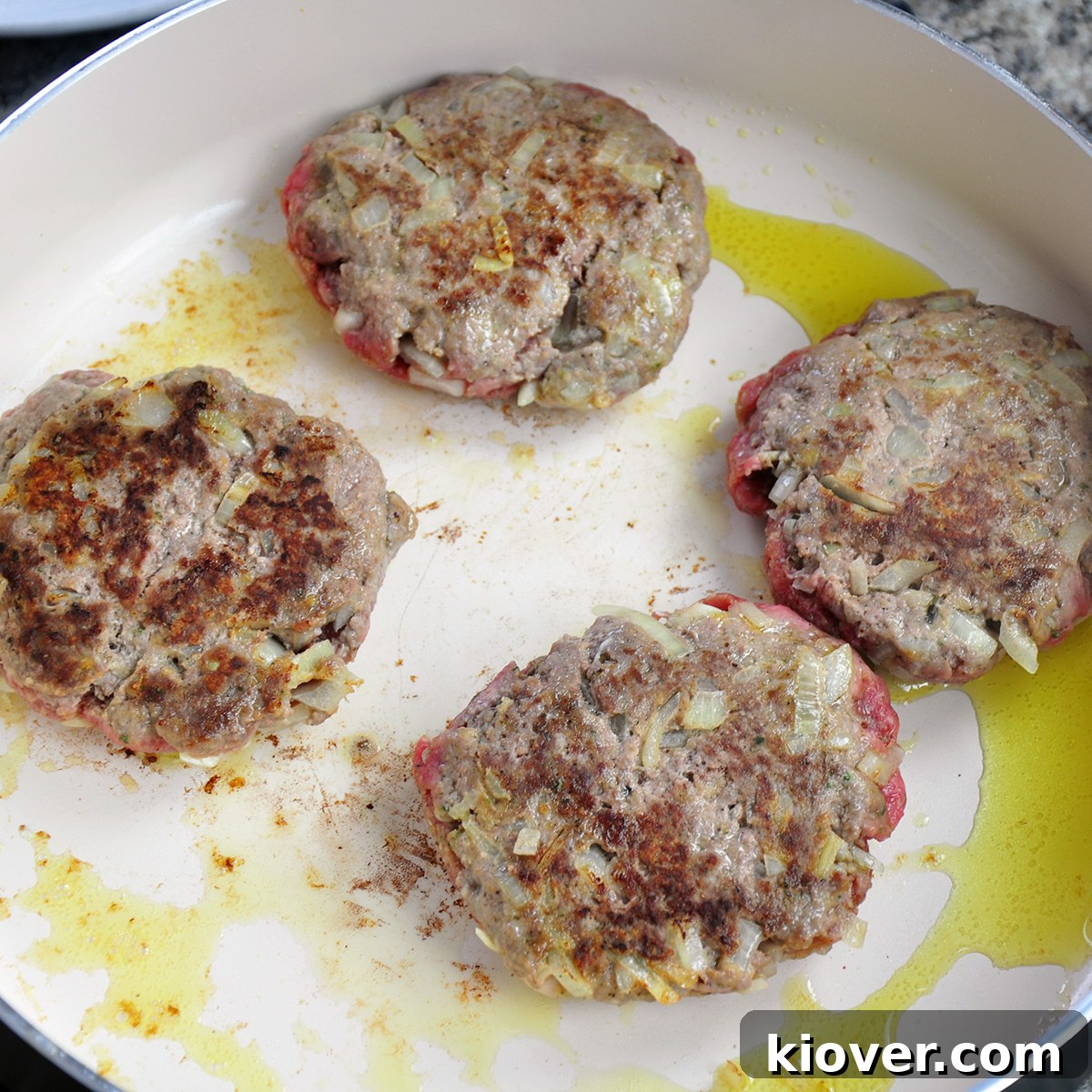 Frying Salisbury Steak Patties Four salisbury steaks frying in a fry pan, developing a golden-brown crust.