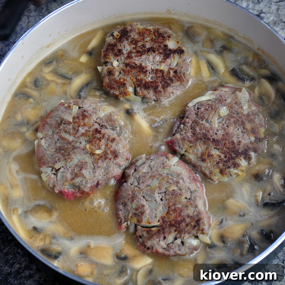 Simmering Salisbury Steaks in Gravy Four steak patties simmering in a saute pan with the mushroom gravy.