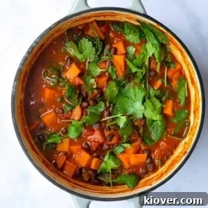 Sweet Potato and Black Bean Stew served in a large pot topped with coriander. The pot is displayed on a white marble background.