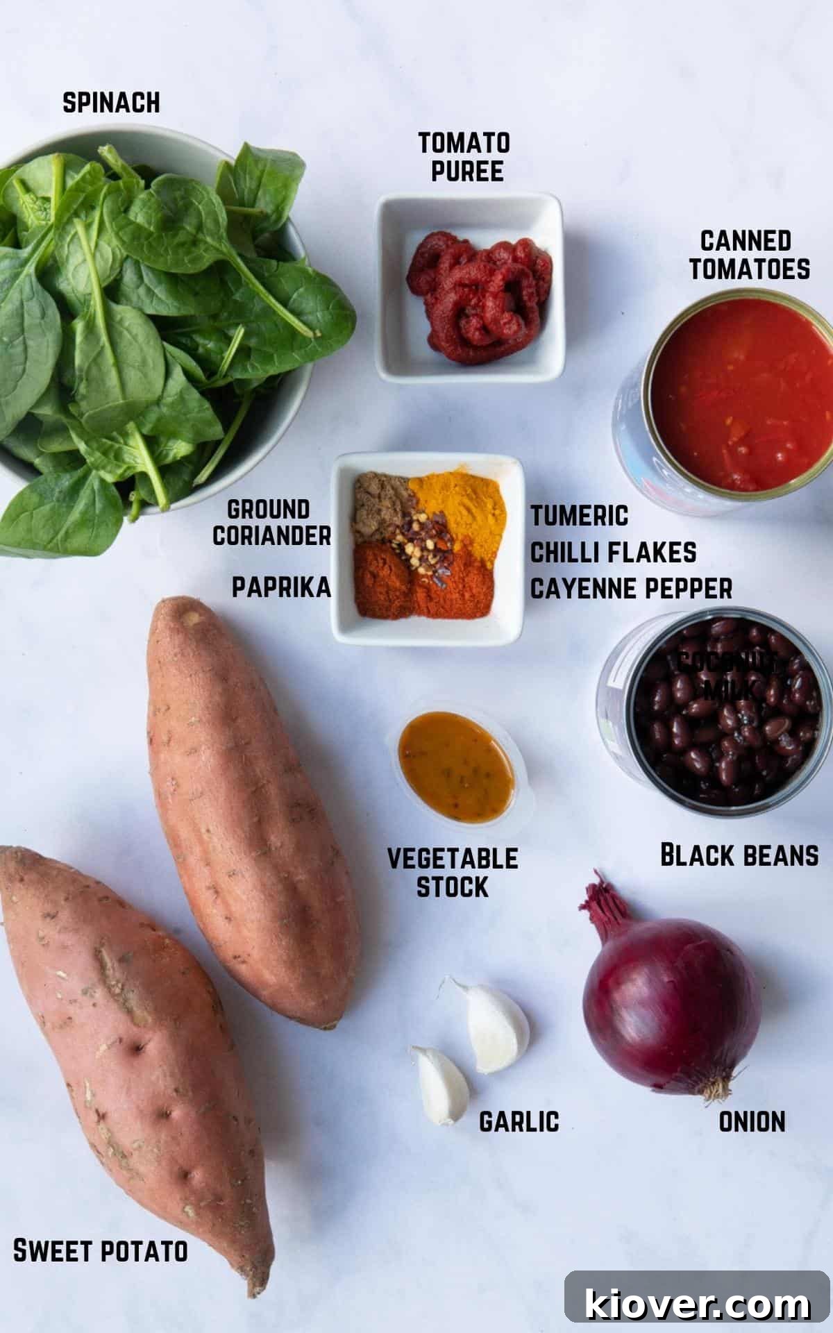 Hearty Sweet Potato and Black Bean Stew 3 A collection of fresh ingredients for Sweet Potato and Black Bean Curry, including sweet potatoes, black beans, spinach, canned tomatoes, and various spices, neatly arranged on a white marble background.