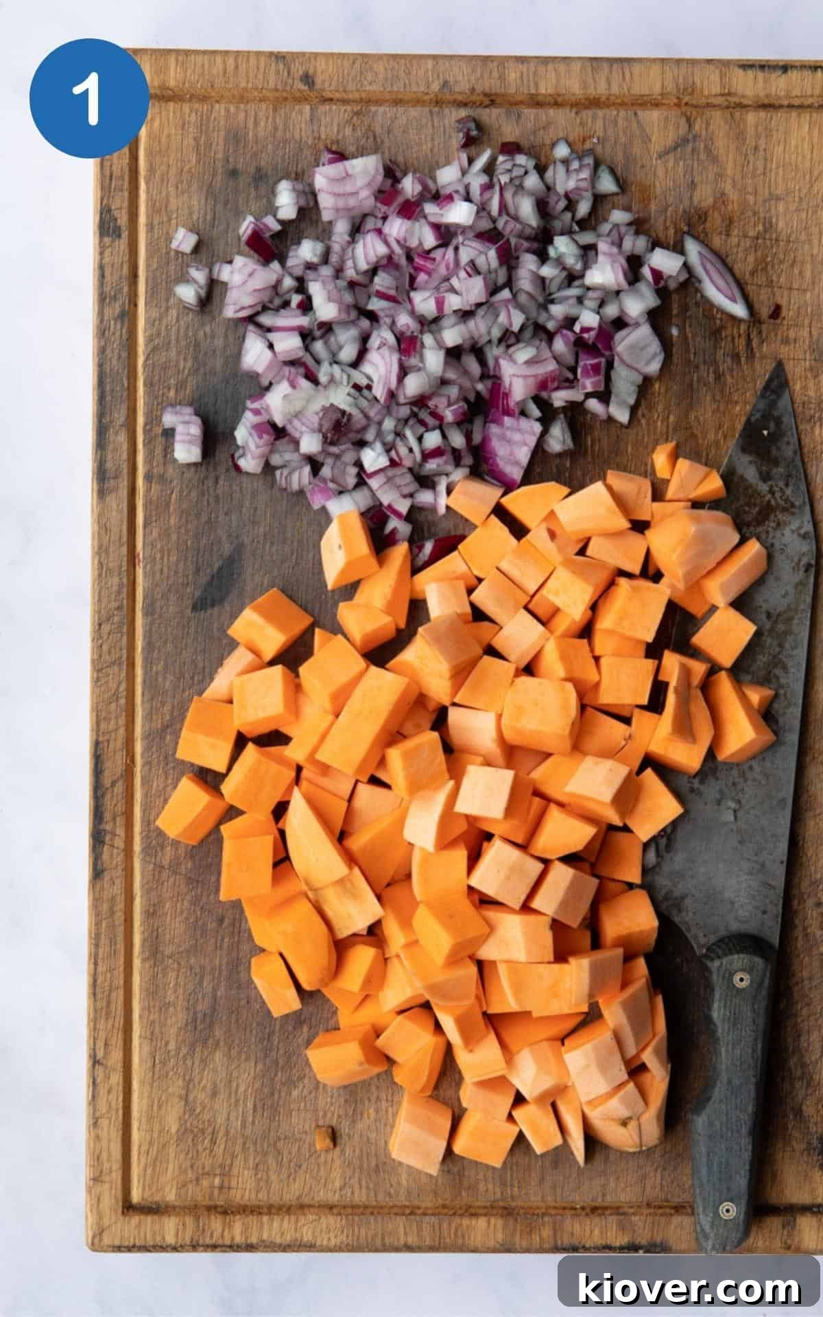 Hearty Sweet Potato and Black Bean Stew 4 Peeled and diced sweet potato and finely chopped red onion on a rustic wooden chopping board, alongside a sharp knife, on a white marble surface.