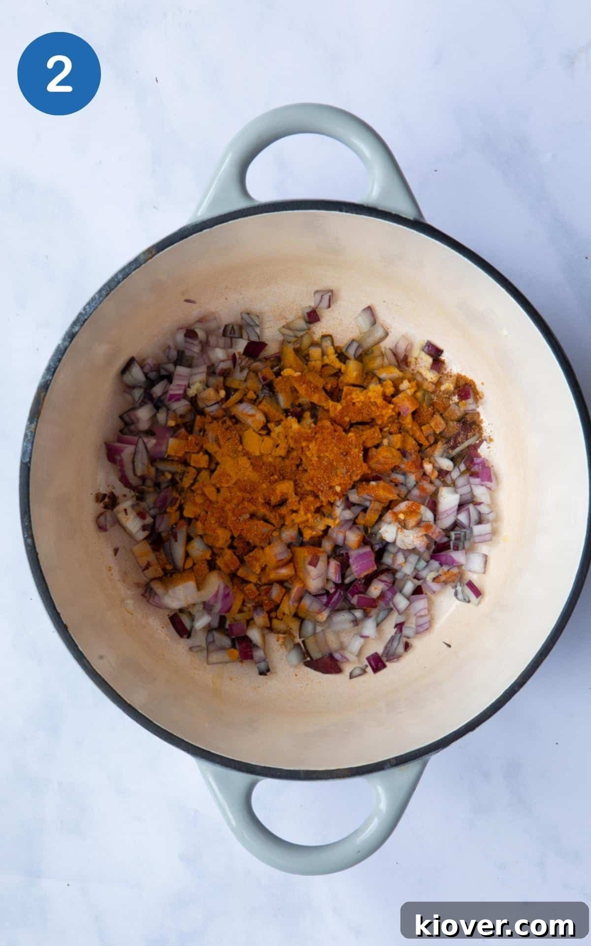 Hearty Sweet Potato and Black Bean Stew 5 A large pot on a white marble background containing sautéed onion, crushed garlic, and a blend of aromatic spices, gently sizzling in olive oil.