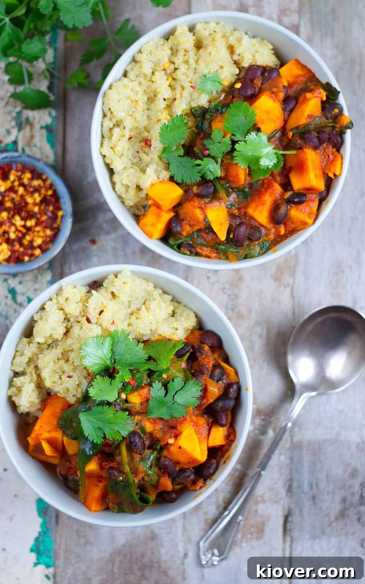Hearty Sweet Potato and Black Bean Stew 8 Two inviting bowls of Sweet Potato and Black Bean Stew, garnished with fresh herbs, ready to be enjoyed on a rustic wooden pallet. A spoon and a small bowl of chilli flakes for optional extra spice complete the appealing presentation.