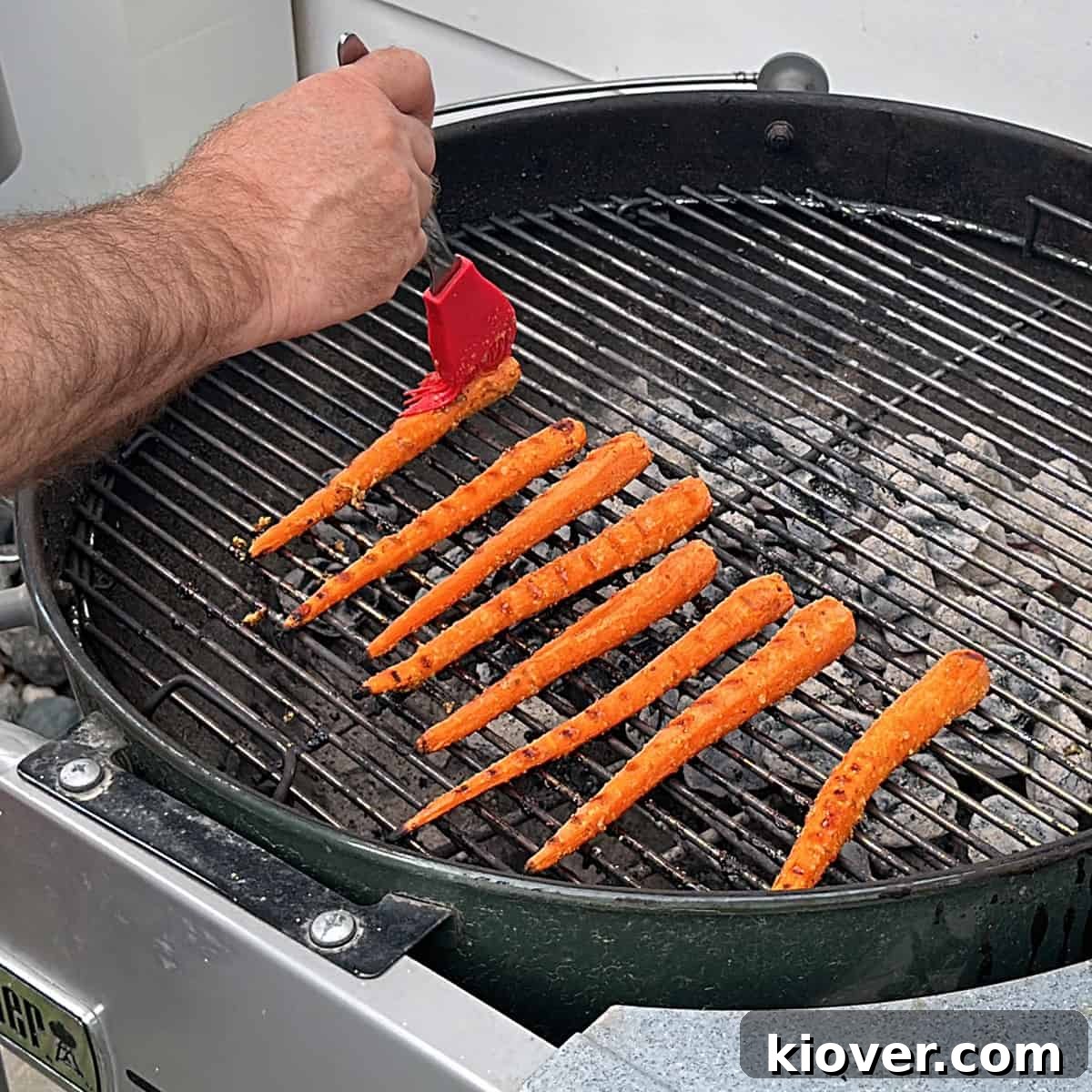 Glazing Carrots on Grill Carrots on a grill with a hand wiping a glaze on the carrots.