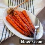 Grilled Carrots on a white plate with a fork and honey spoon.