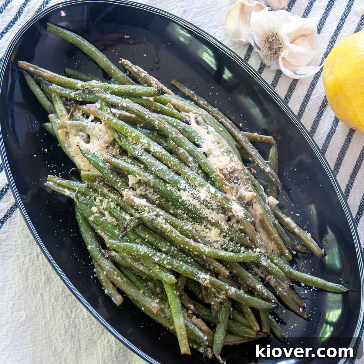 Perfectly grilled green beans, beautifully charred and topped with grated Parmesan cheese, served on a dark plate.