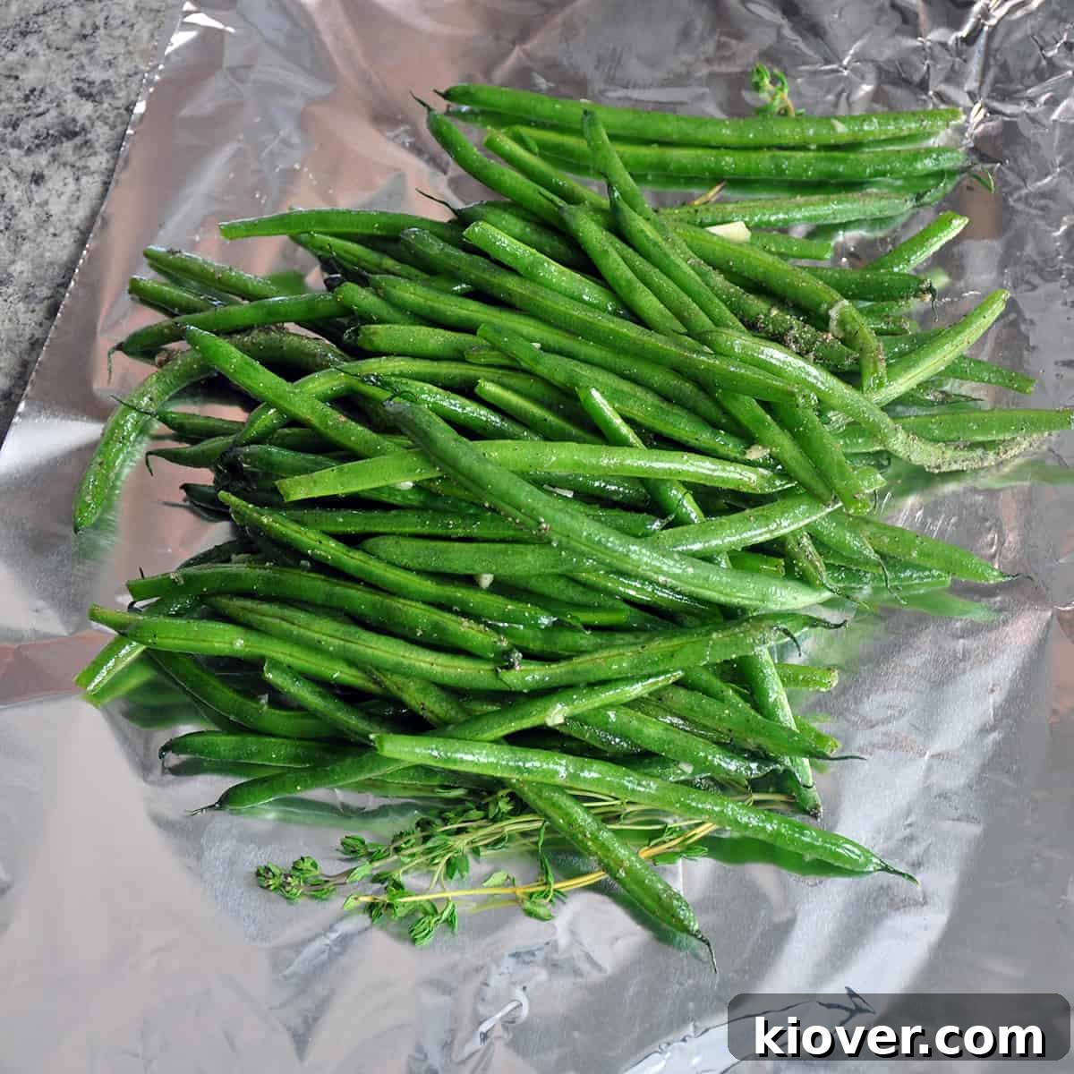 Fresh green beans and thyme sprigs arranged on a piece of tinfoil, ready for seasoning.