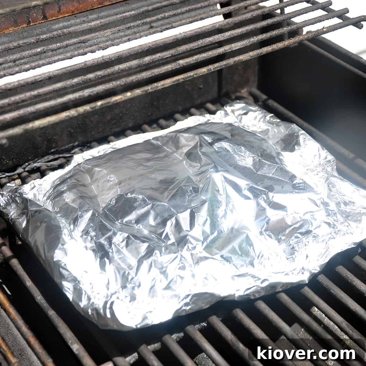 A foil packet of green beans cooking on the grates of a Weber grill, showing the direct heat method.