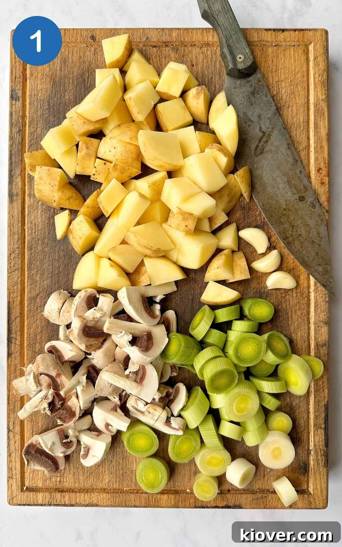 Freshly chopped potatoes, sliced mushrooms, and neatly cut leeks are arranged on a rustic wooden chopping board, ready for the first steps of the Vegan Mushroom Pie recipe.