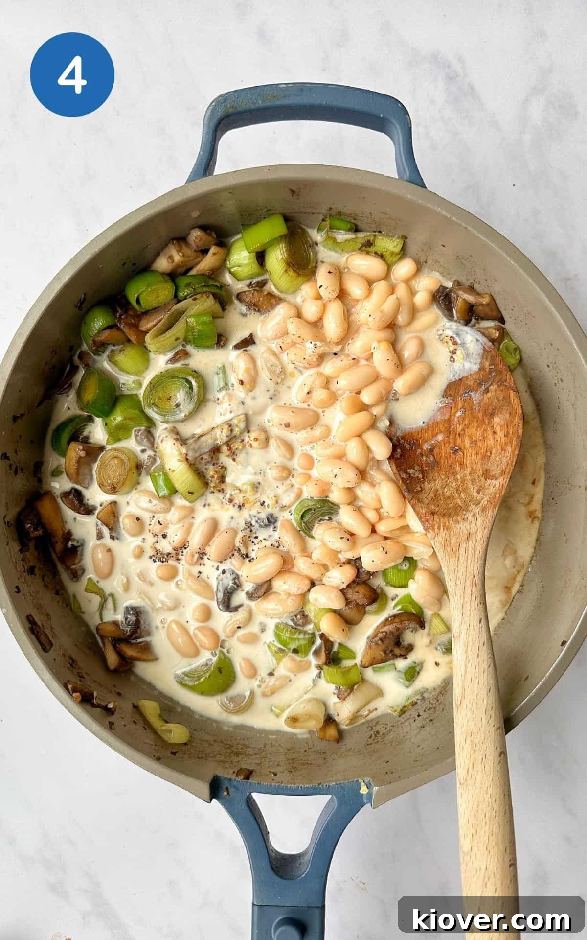 A creamy, savory mixture of sautéed mushrooms, leeks, and cannellini beans simmers gently in a frying pan, enriched with soya cream and wholegrain mustard, forming the delicious pie filling.
