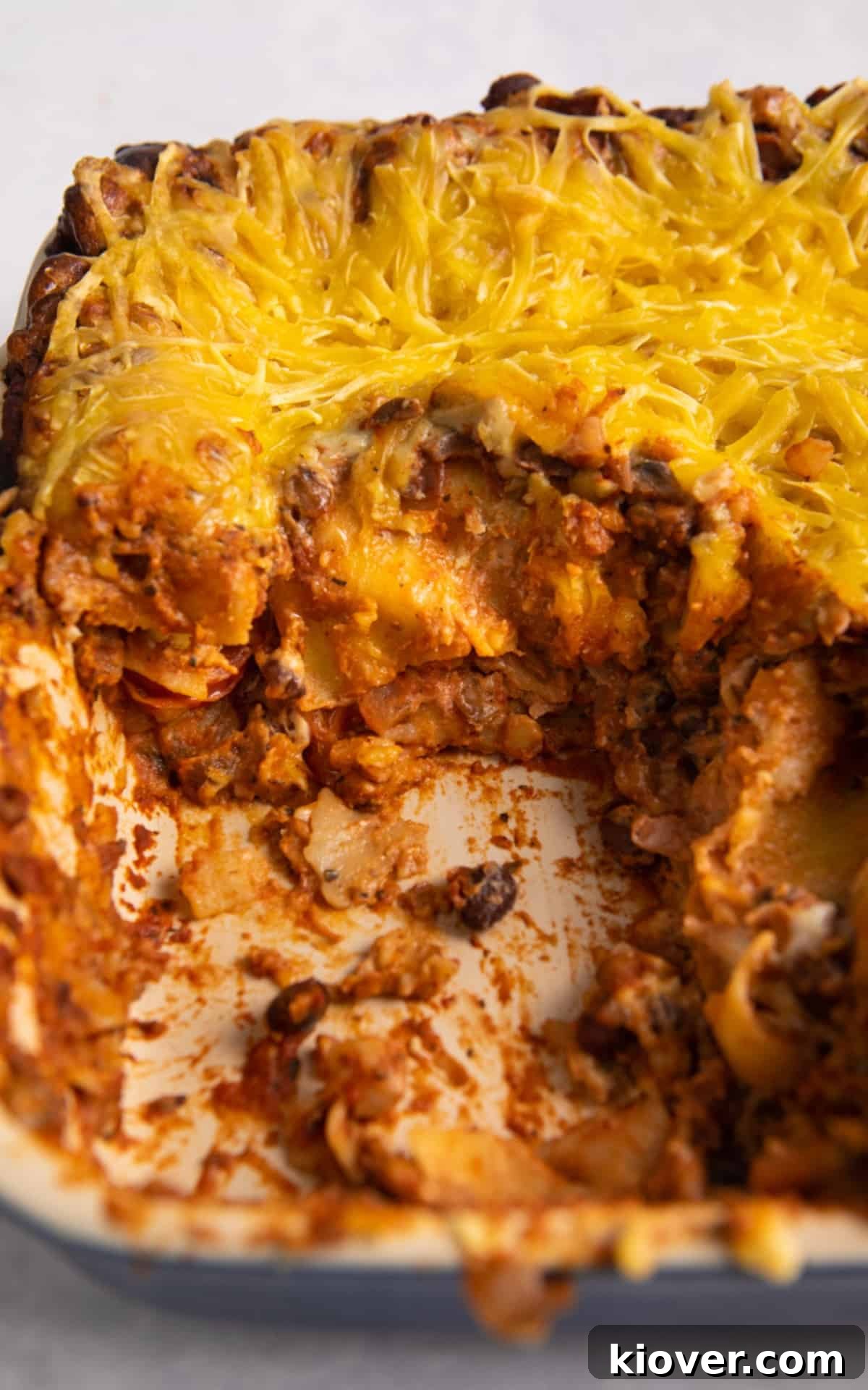 Plant-Based Lasagne Perfection 11 A large baking dish of freshly baked vegan lasagne with a slice missing, showing the beautiful layers of pasta, red sauce, and creamy béchamel, on a white background.