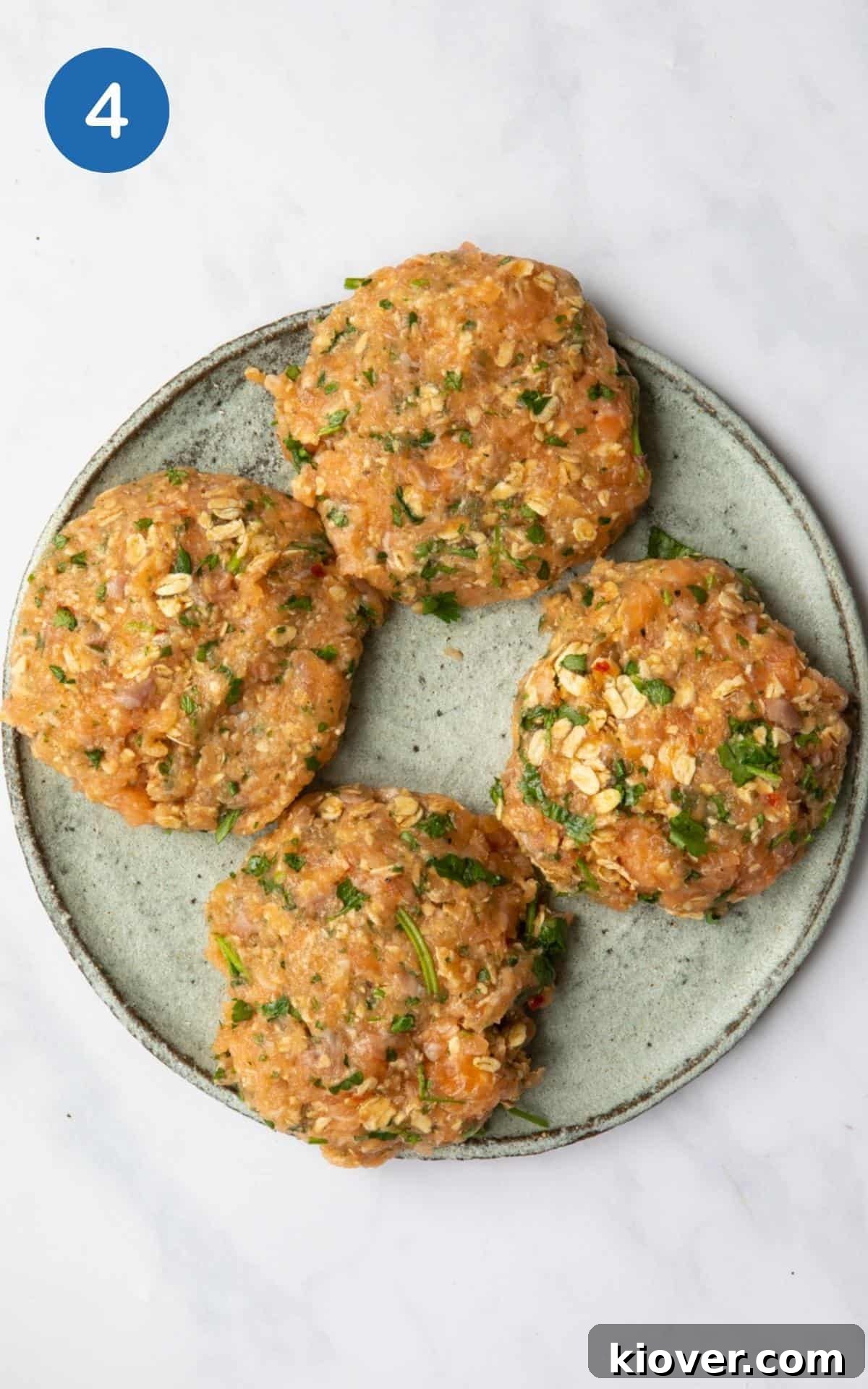 Several uncooked Sweet Chilli Salmon Fishcakes, perfectly formed into uniform patty shapes, arranged on a vibrant blue plate against a clean white marble background, ready for cooking.