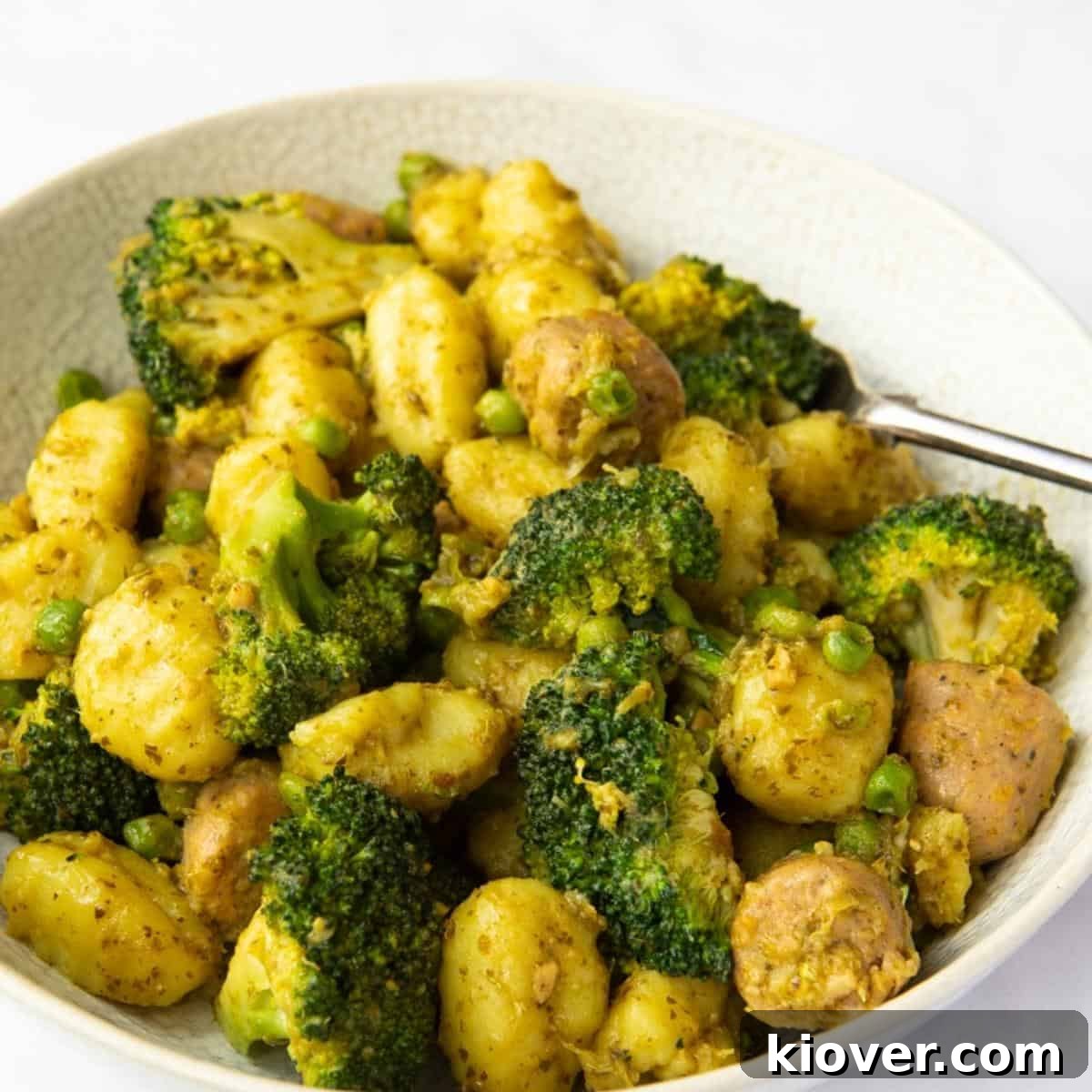 Savory Sausage Pesto Gnocchi 2 Image shows a close up of Sausage Pesto Gnocchi served in a bowl with a white background, garnished with fresh herbs.