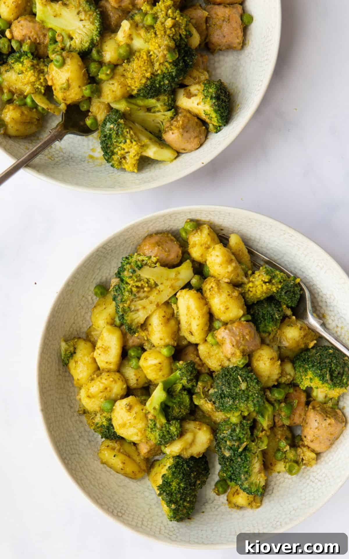 Savory Sausage Pesto Gnocchi 9 Image shows 2 bowls of Sausage Gnocchi Pasta ready to eat with forks. Bowls are displayed on a white marble background, indicating a serving suggestion for the delicious meal.