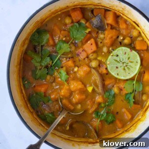 Sweet Potato Satay Curry displayed in a large pot with a serving spoon. The pot is on a white marble background, indicating a healthy and delicious meal.