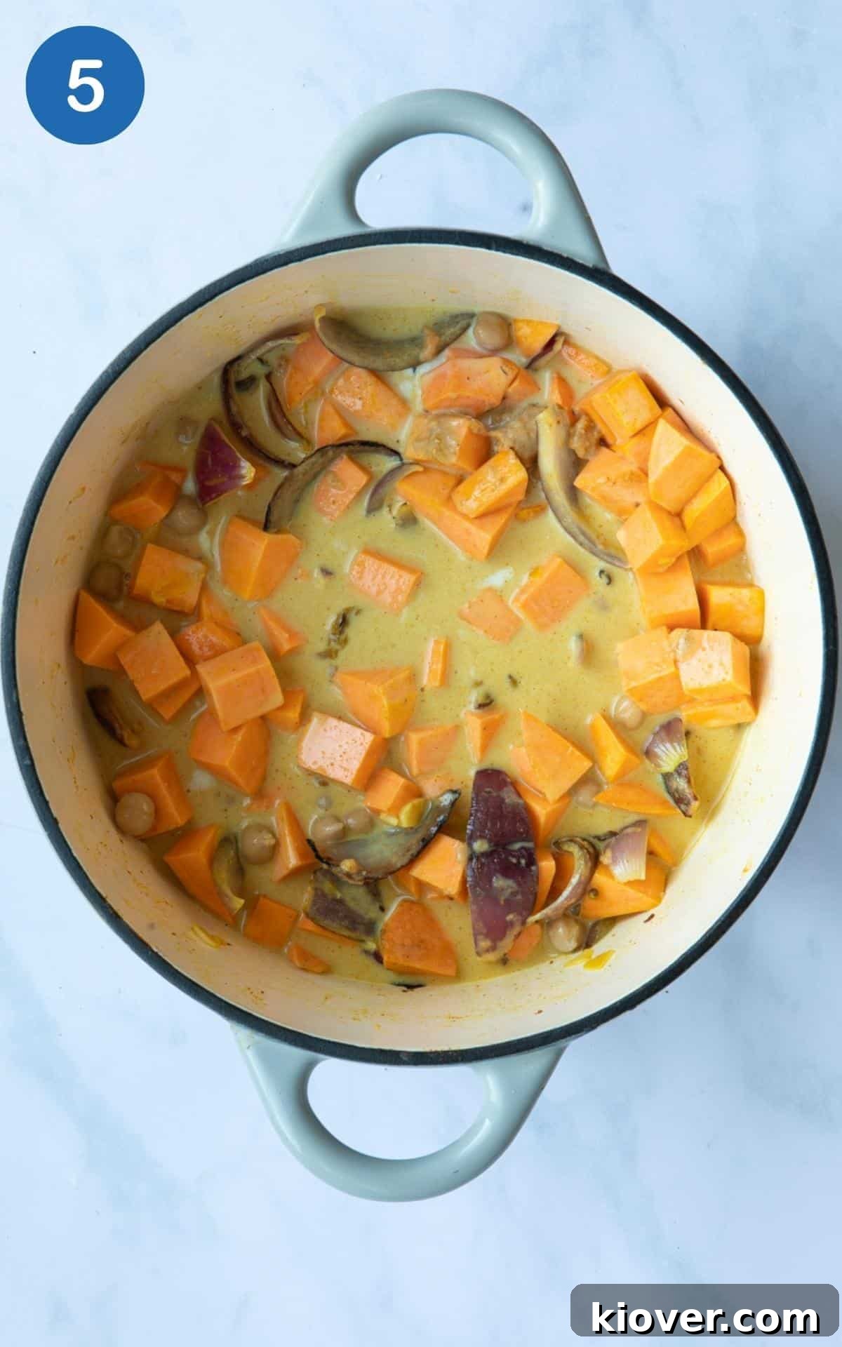 Ingredients simmering gently in a large oven-proof pot, releasing steam. The pot is displayed on a white marble background, ready for the oven.