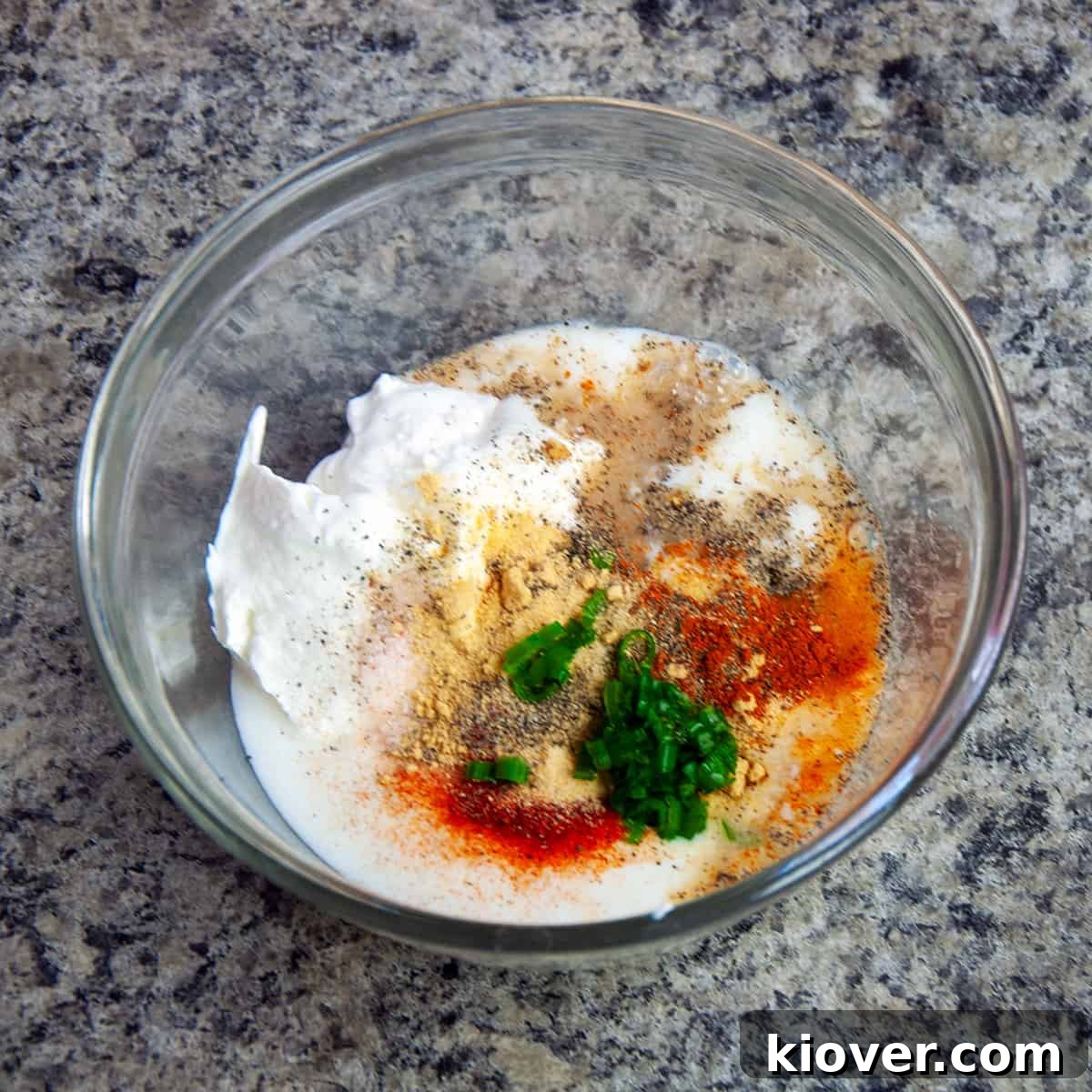 Unmixed sour cream dip ingredients in a glass bowl, showcasing the distinct layers before blending.