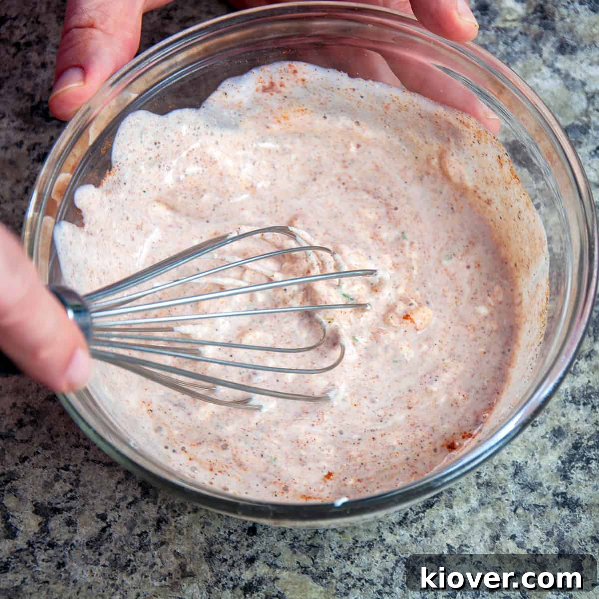 A whisk blending the sour cream dip ingredients in a clear glass bowl, showing the creamy texture.