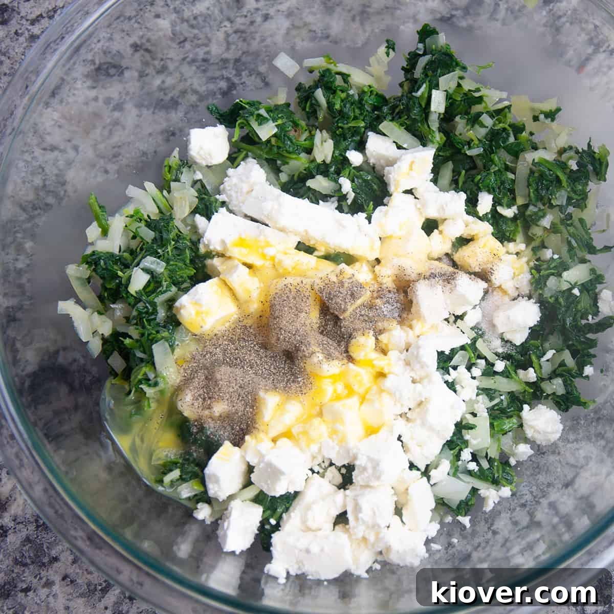 Big glass bowl with feta, eggs, salt, pepper, and spinach mix.