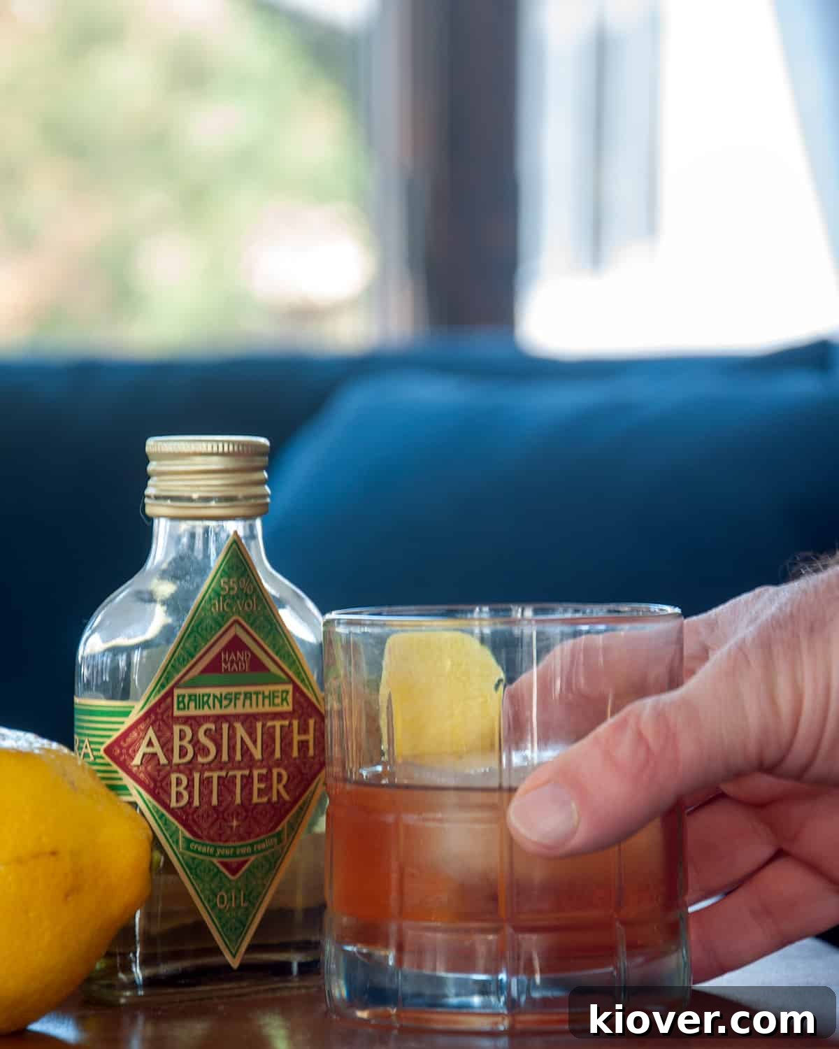 A hand holding a classic Sazerac cocktail with a lemon twist.