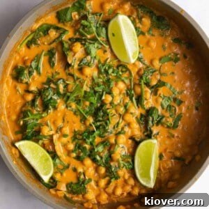chickpea curry topped with fresh lime wedges and freshly chopped coriander in large pan.