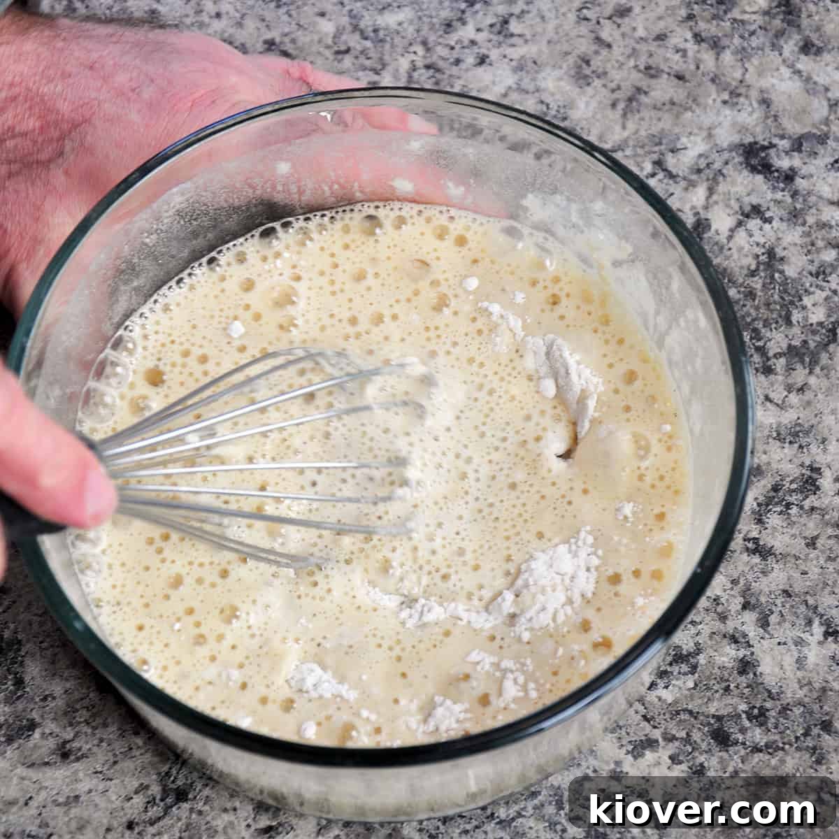 A whisk blending flour, buttermilk, and beer together in a bowl to create a smooth batter.