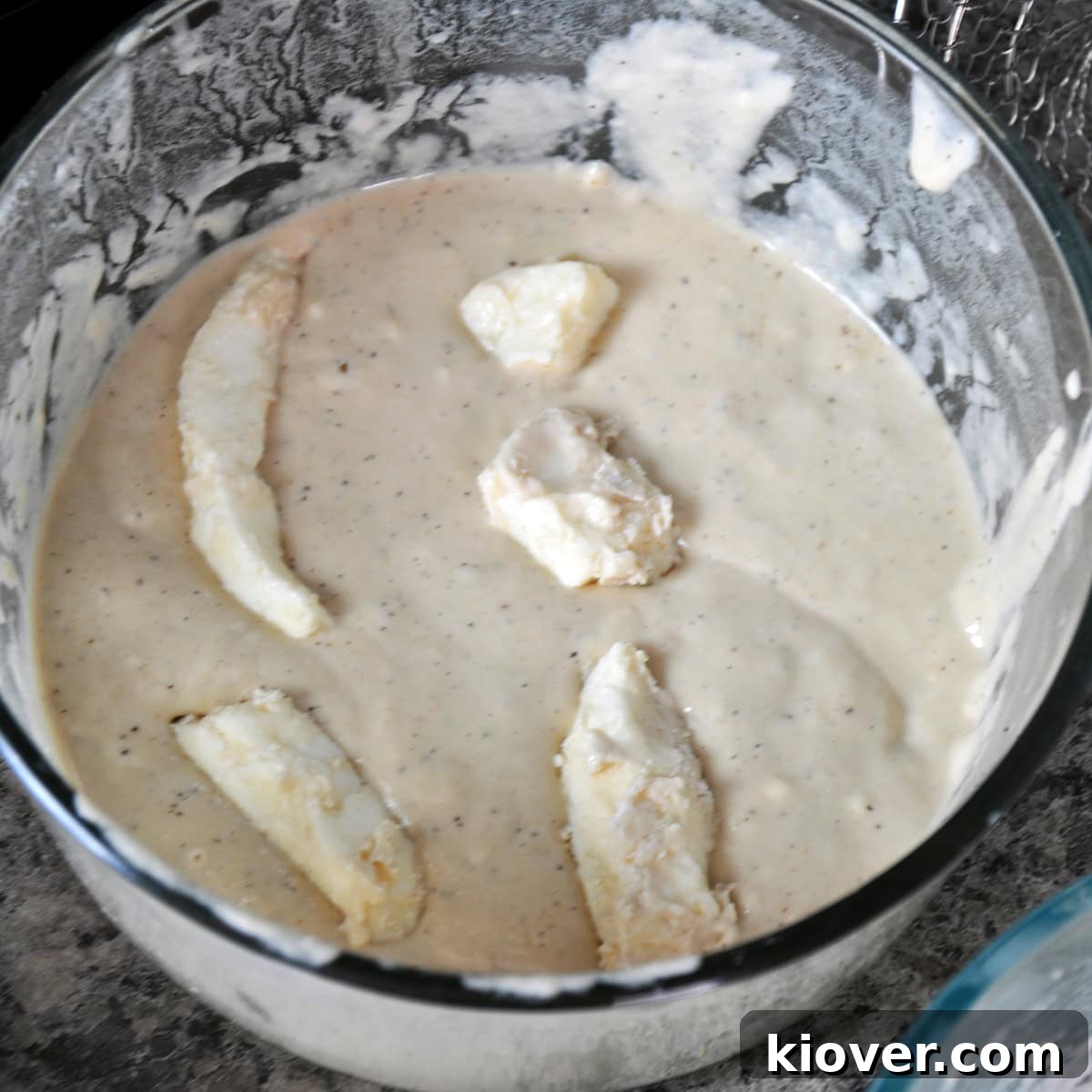 Several cheese curds submerged in the batter, ready for frying.
