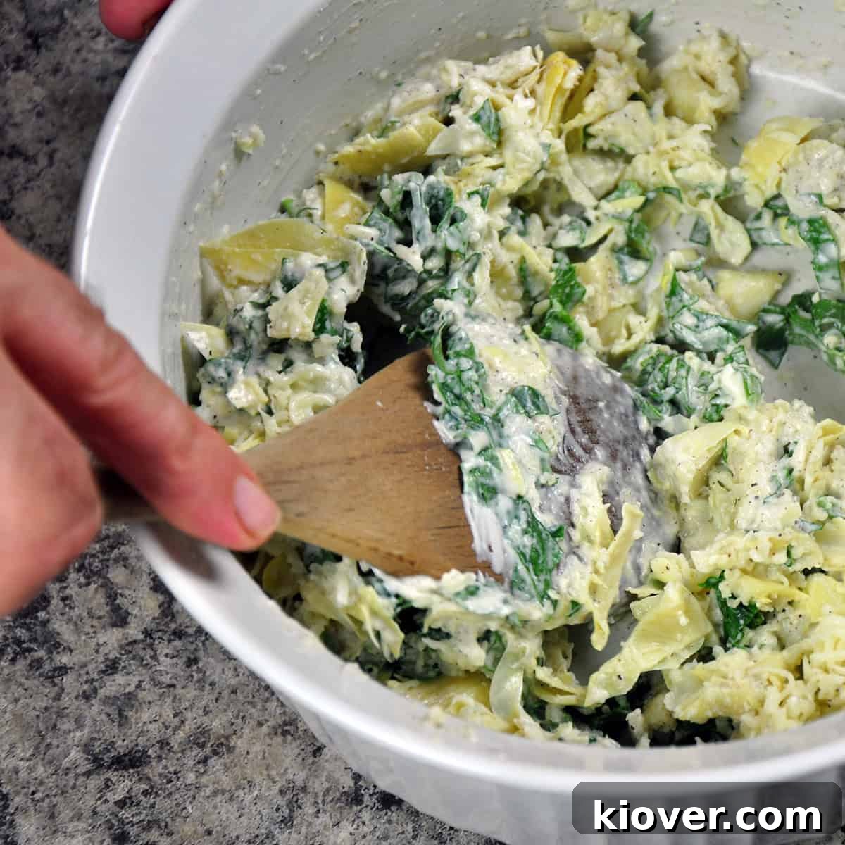 Artichoke Filling Mixing A wooden spoon stirring the creamy artichoke dip filling in a bowl, showing the smooth consistency and blended ingredients.