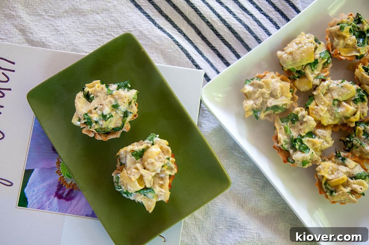 Artichoke Dip Phyllo Cup Two perfectly golden Spinach and Artichoke Dip Phyllo Cups arranged elegantly on a green plate, with several more delicious cups blurred in the background, ready for serving.
